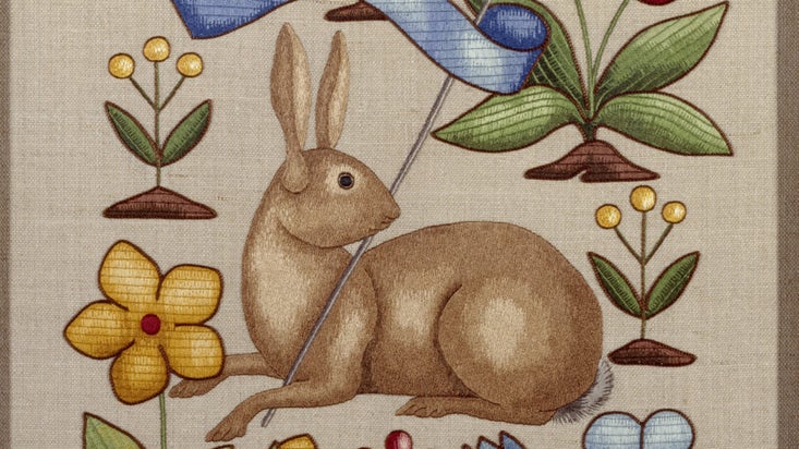 Detail of embroidered panel by Joan Lander in the collection at Sunnycroft, featuring a design of a rabbit holding a pennant surrounded by stylized flowers